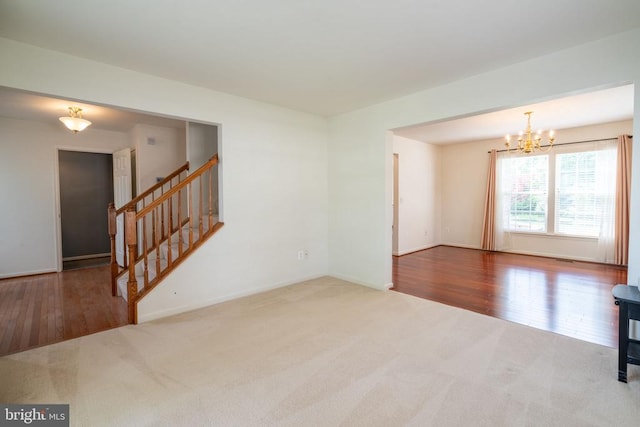 unfurnished living room with carpet floors, a chandelier, stairway, baseboards, and wood finished floors