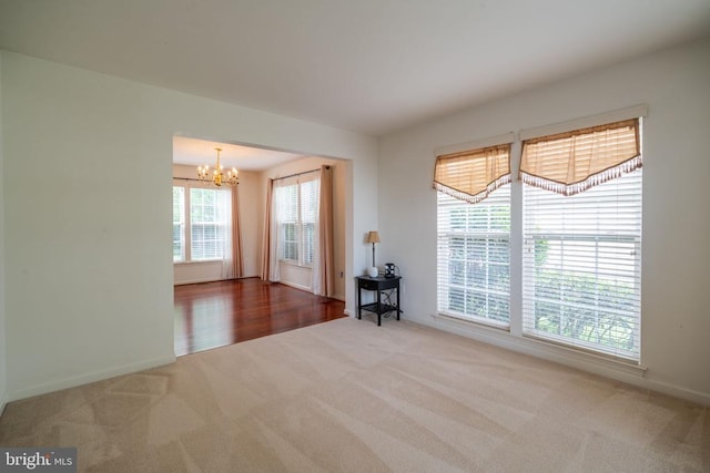 spare room featuring carpet floors, a chandelier, and baseboards