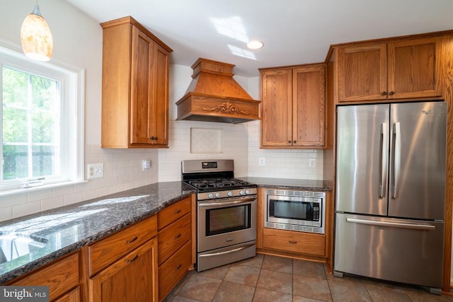 kitchen featuring appliances with stainless steel finishes, custom range hood, brown cabinets, and decorative backsplash