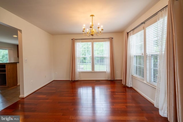 unfurnished dining area with a chandelier, healthy amount of natural light, and wood finished floors