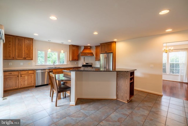kitchen with stainless steel appliances, custom exhaust hood, brown cabinetry, a center island, and a sink
