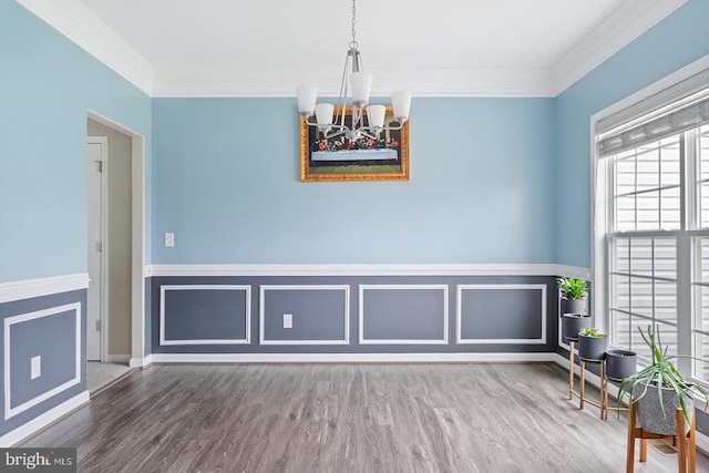 unfurnished dining area with wood finished floors, baseboards, wainscoting, a chandelier, and ornamental molding