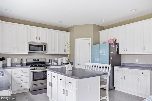 kitchen featuring light tile patterned floors, white cabinetry, a kitchen island, dark countertops, and appliances with stainless steel finishes