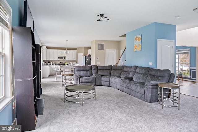 living room featuring stairway, visible vents, and light colored carpet