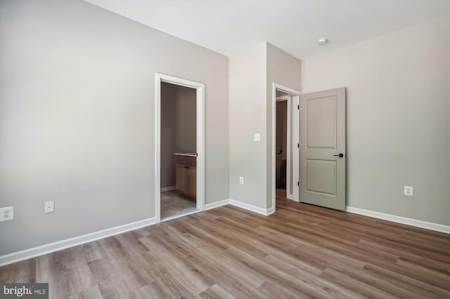  - unfurnished bedroom with wood finished floors, baseboards, and connected bathroom
