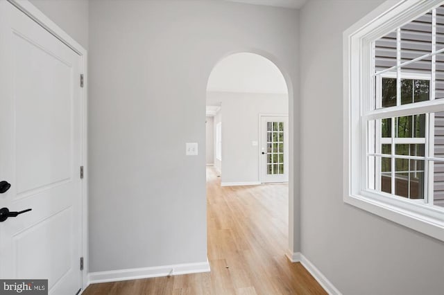  - corridor featuring light wood-style floors, arched walkways, and baseboards