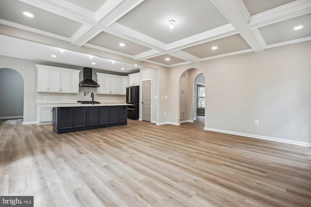  - kitchen with arched walkways, wall chimney range hood, black fridge, coffered ceiling, and open floor plan