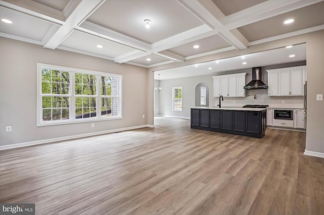  - kitchen featuring coffered ceiling, wall chimney exhaust hood, open floor plan, white cabinetry, and light countertops