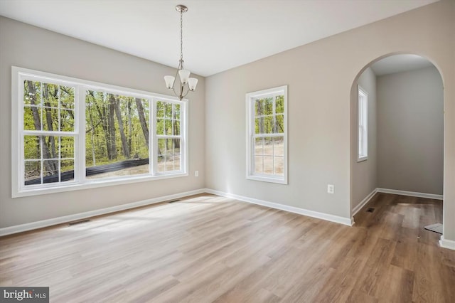  - unfurnished dining area featuring wood finished floors, baseboards, arched walkways, and a chandelier