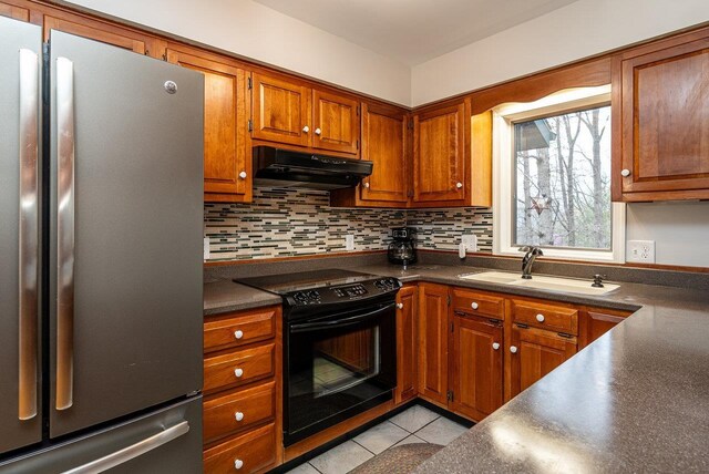 kitchen featuring freestanding refrigerator, under cabinet range hood, black electric range oven, a sink, and dark countertops