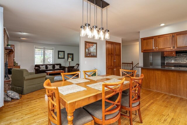 dining room with light wood-style flooring, a brick fireplace, a chandelier, and recessed lighting