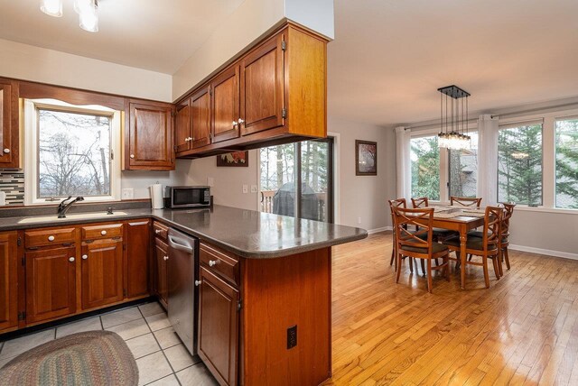 kitchen with a sink, appliances with stainless steel finishes, dark countertops, a peninsula, and brown cabinets