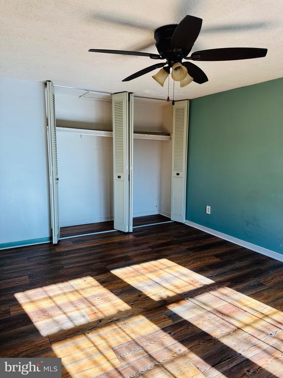 unfurnished bedroom with dark wood-type flooring, baseboards, multiple closets, and ceiling fan