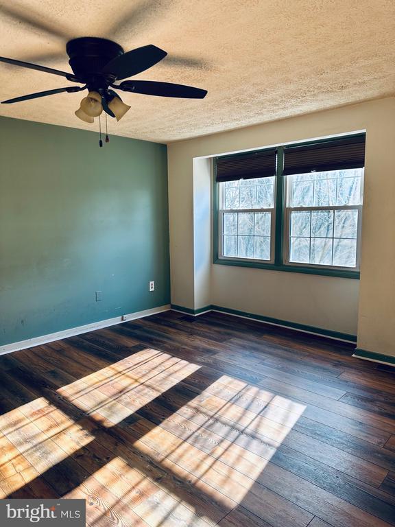 unfurnished room featuring ceiling fan, a textured ceiling, baseboards, and hardwood / wood-style floors