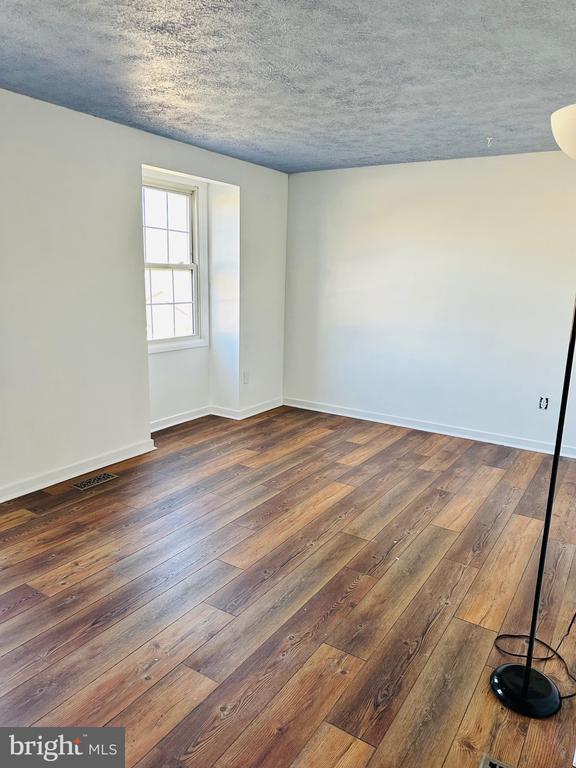 empty room with visible vents, baseboards, a textured ceiling, and dark wood-style flooring