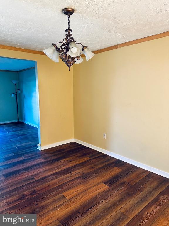 empty room featuring a notable chandelier, wood finished floors, baseboards, and a textured ceiling