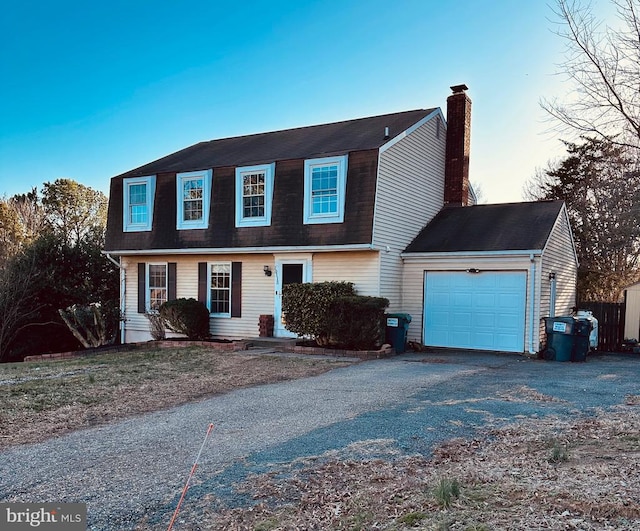 colonial inspired home featuring aphalt driveway, a gambrel roof, an attached garage, and a chimney