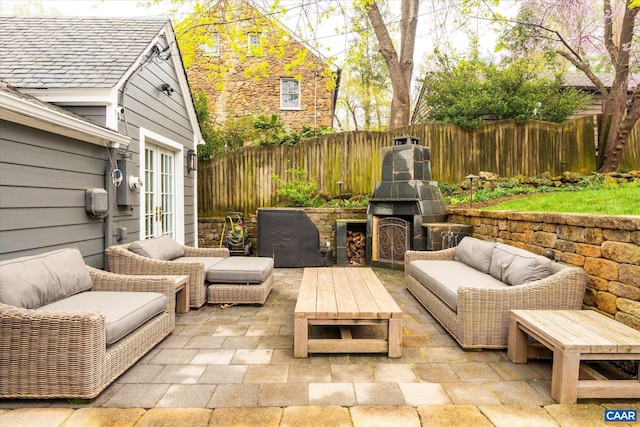 view of patio with a fenced backyard, an outdoor living space with a fireplace, and french doors