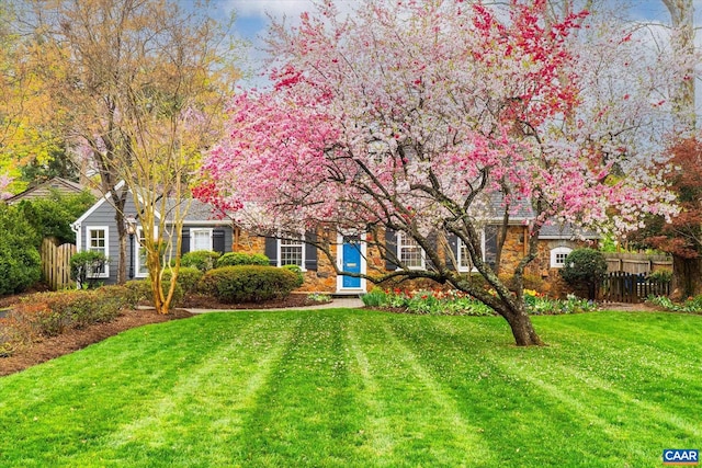 view of property hidden behind natural elements featuring stone siding, fence, and a front yard