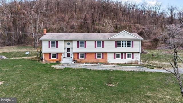 split foyer home with a chimney, brick siding, a front lawn, and a view of trees