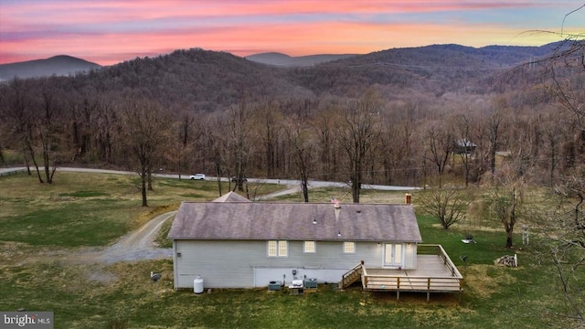 back of property at dusk featuring a deck with mountain view, a forest view, and a yard