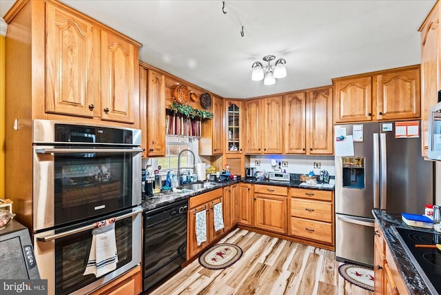kitchen featuring black appliances, a sink, glass insert cabinets, light wood-style flooring, and dark stone counters