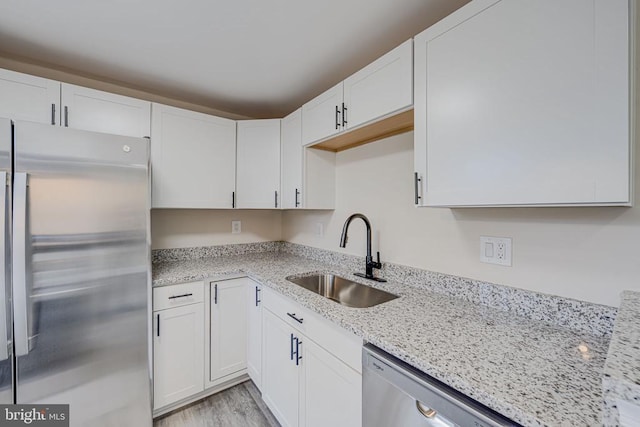 kitchen featuring a sink, appliances with stainless steel finishes, light stone counters, white cabinets, and light wood-style floors