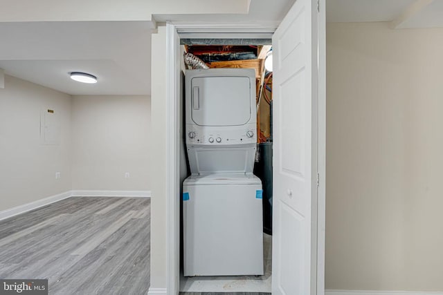 clothes washing area with laundry area, stacked washing maching and dryer, wood finished floors, and baseboards