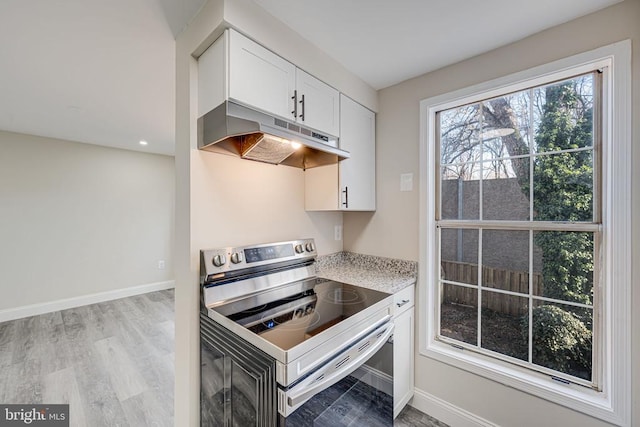 kitchen featuring light wood finished floors, white cabinets, baseboards, stainless steel electric stove, and under cabinet range hood