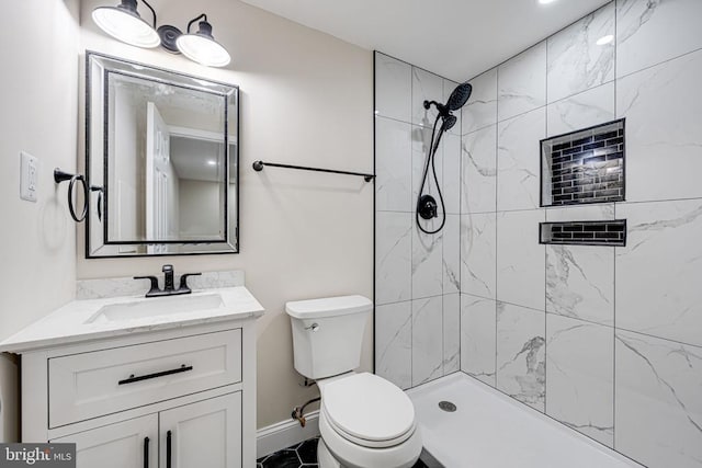 full bath featuring toilet, a tile shower, vanity, and baseboards