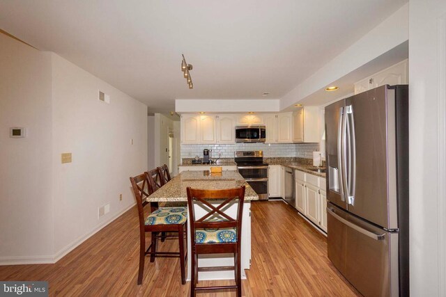 11523 Red Rock Ln, Bumpass, VA 23024 - kitchen featuring stainless steel appliances, tasteful backsplash, light wood-type flooring, light stone countertops, and a kitchen breakfast bar