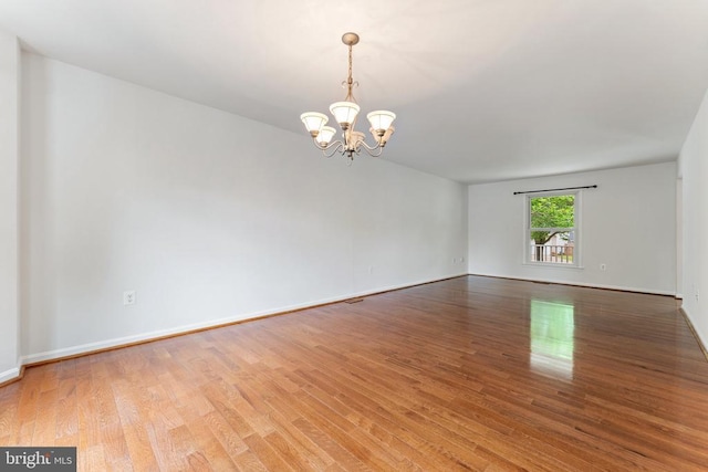 spare room with a chandelier, wood finished floors, and baseboards