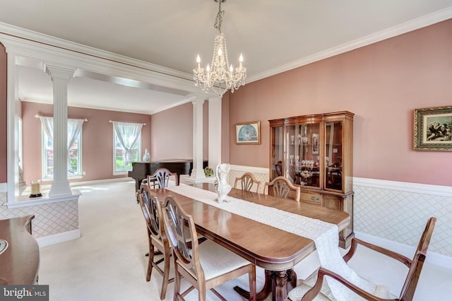carpeted dining area with ornate columns, wainscoting, crown molding, and a chandelier