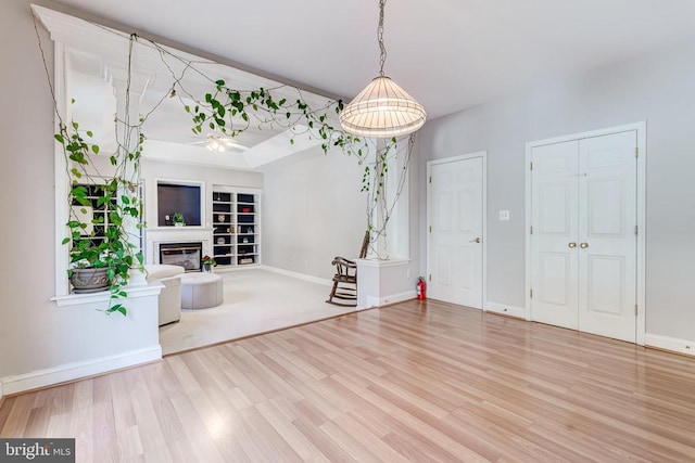 unfurnished living room with wood finished floors, built in shelves, baseboards, and a glass covered fireplace
