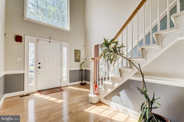 entrance foyer featuring a towering ceiling, wood finished floors, stairway, and baseboards