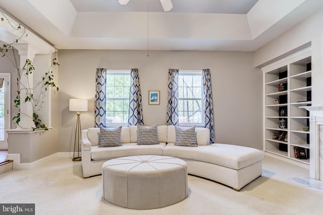 living area featuring carpet floors, a tray ceiling, a ceiling fan, and baseboards