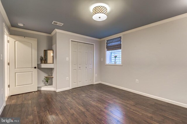 unfurnished bedroom featuring dark wood finished floors, baseboards, crown molding, and a closet