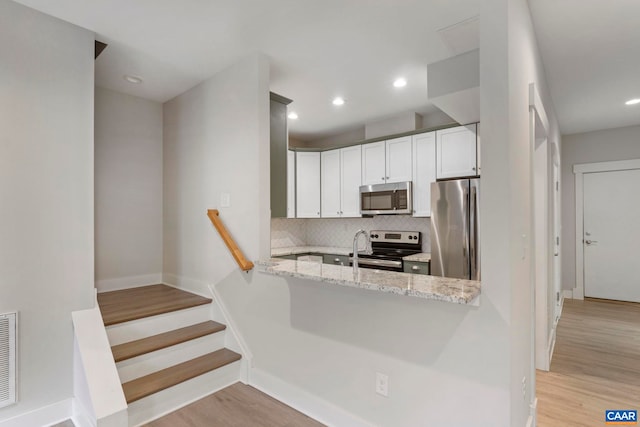 kitchen with stainless steel appliances, light wood-type flooring, backsplash, white cabinetry, and light stone countertops