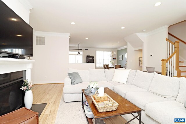 living room featuring a fireplace, crown molding, light wood-type flooring, visible vents, and stairway