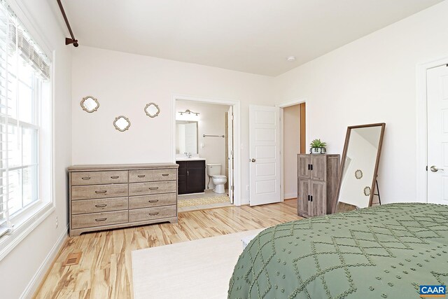 bedroom featuring light wood-style flooring, a sink, ensuite bathroom, visible vents, and baseboards