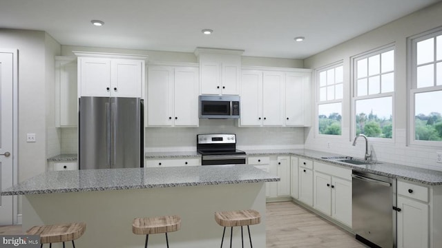 kitchen with stainless steel appliances, a sink, white cabinetry, a center island, and a kitchen bar