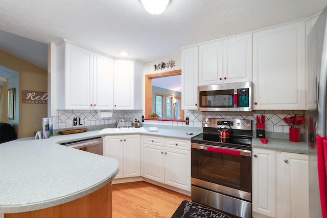 kitchen with white cabinetry, appliances with stainless steel finishes, kitchen peninsula, light hardwood / wood-style floors, and backsplash