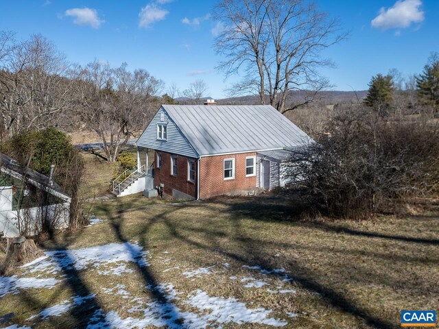 view of property exterior with metal roof, a chimney, brick siding, and a lawn
