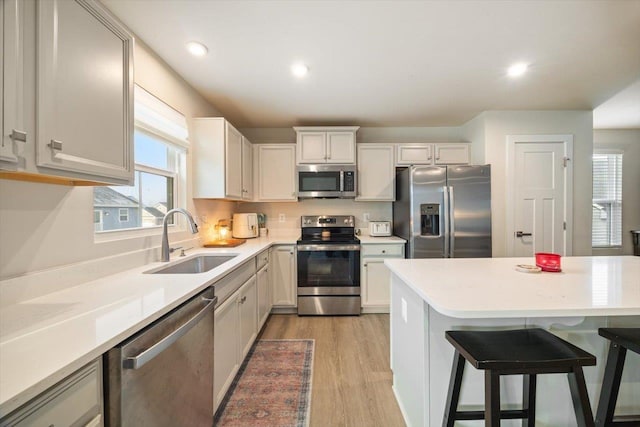 kitchen with a breakfast bar, sink, light hardwood / wood-style flooring, appliances with stainless steel finishes, and white cabinets