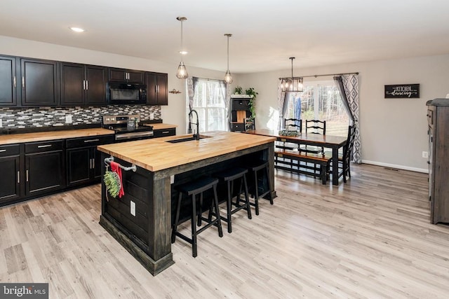 kitchen featuring butcher block countertops, a breakfast bar, electric range, tasteful backsplash, and a center island with sink