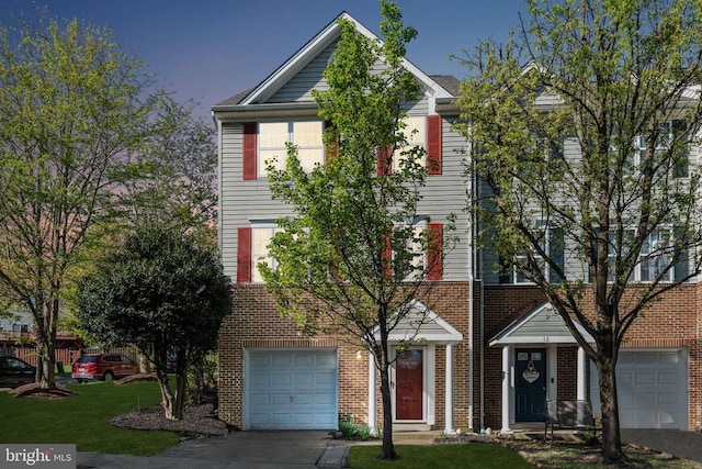 townhome / multi-family property with a front lawn, a garage, driveway, and brick siding