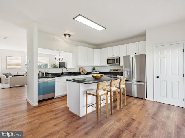 kitchen featuring stainless steel appliances, white cabinets, a breakfast bar area, dark countertops, and a sink