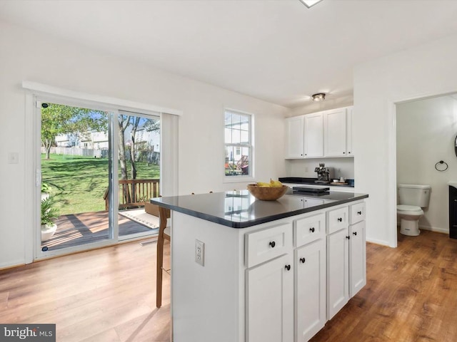 kitchen featuring dark countertops, white cabinets, light wood-style floors, a center island, and a breakfast bar area