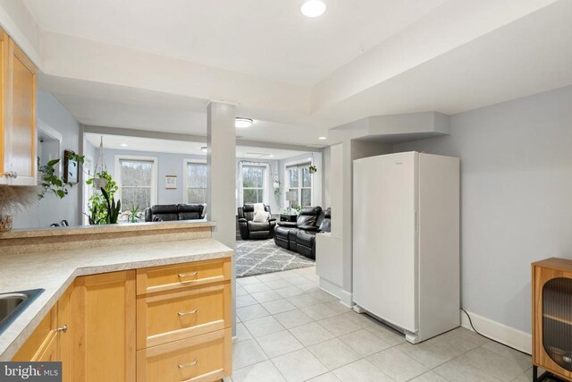 kitchen featuring light brown cabinetry, light tile patterned floors, sink, and white fridge