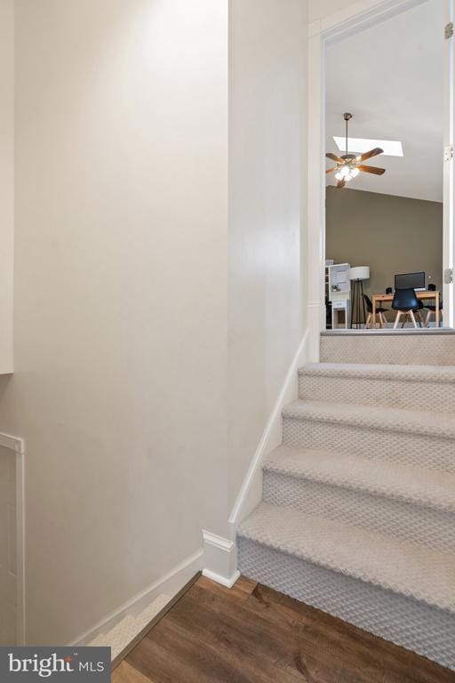 staircase with ceiling fan, wood-type flooring, and vaulted ceiling